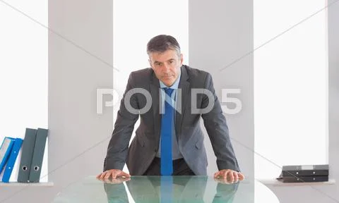 Frowning businessman standing in front of a desk Stock Photos