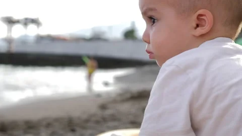 Frowning one year old boy in white t-shirt playing with pebbles on Black sea Stock Footage 221862842