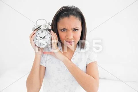 Frowning young dark haired model holding an alarm clock Stock Photos