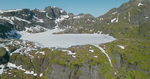 Frozen Alpine Lake Surrounded by Granite Peaks under blue sky in Lofoten Vidéo 334089115