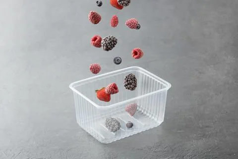 Frozen berries fall into a plastic box on a grey concrete background. Foto stock