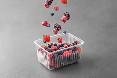 Frozen berries fall into a plastic box on a grey concrete background. Stock Photos