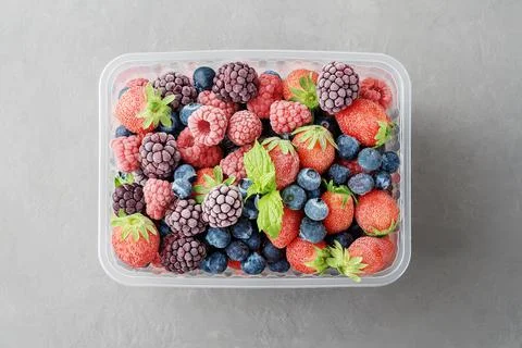 Frozen berries in a plastic box on a grey concrete background. Stock Photos