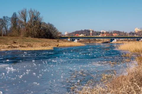 A frozen blue river with bits of ice on the surface. Reeds along the banks .. Stock Photos
