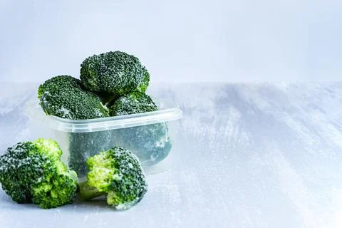 Frozen broccoli in a plastic box on grey table, copy space Stock Photos