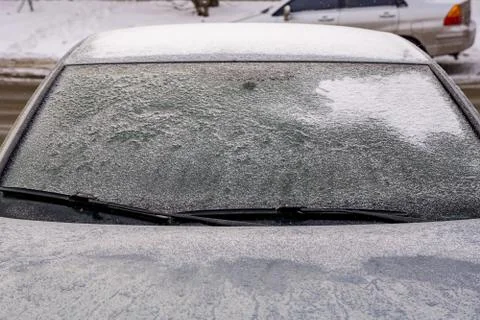 Frozen car windshield covered with ice and snow on a winter day. Close-up view. Stock Photos