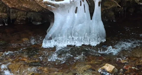 A frozen cascade drapes a mossy branch over the water. The ice glistens above Stock Footage 324866393