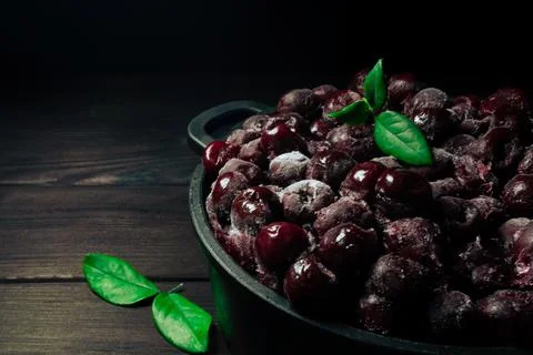 Frozen cherry in a bowl with green leaf on a wooden black background.Vitamins Stock-Fotos