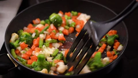 Frozen chopped vegetables are cooked in frying pan and stirred with spatula Stock Footage 232780457
