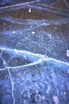 Frozen Ice Cracks and Bubbles Over Rocky Lakebed Winter Texture Close Up Stock Photos