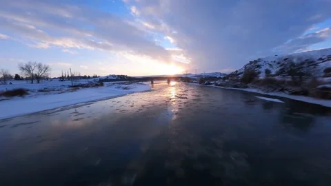 Frozen ice river winter sunset aerial shot with fpv drone rocky mountain scene Stock Footage 156570937
