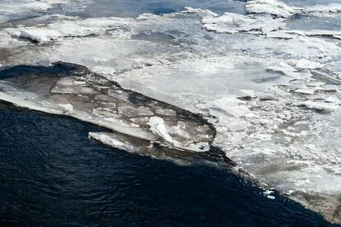 Frozen ice sheets break apart on the surface of a dark, cold river, depicting Stock Photos