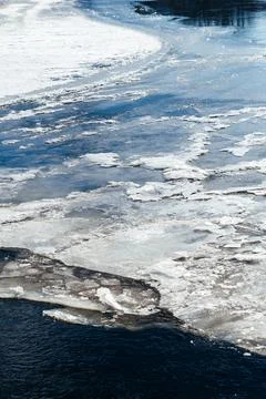 Frozen ice sheets break apart on the surface of a dark, cold river, depicting Stock Photos
