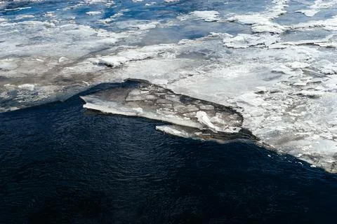 Frozen ice sheets break apart on the surface of a dark, cold river, depicting Stock Photos