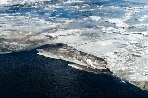 Frozen ice sheets break apart on the surface of a dark, cold river, depicting Stock Photos