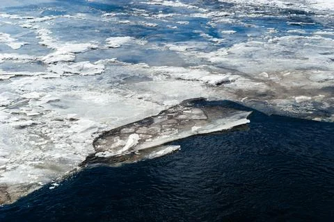 Frozen ice sheets break apart on the surface of a dark, cold river, depicting Stock Photos