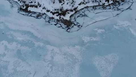 Frozen lake with cracked ice in winter, with snow on the ice and the coast. Stock Footage 106924802