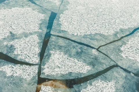 A frozen lake has various cracks and shapes in the ice. Some areas are clear  Stock Photos