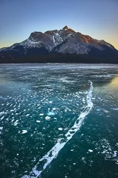 Frozen Lake Ice Patterns and Snow Capped Mountain at Sunrise in Winter Stock Photos