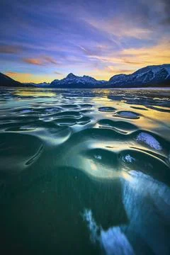 Frozen Lake Ice Patterns at Sunset with Dramatic Mountain Skyline Winter La.. 스톡 사진