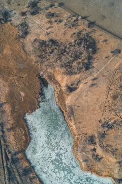 Frozen lake with icy patterns surrounded by dry brown meadows barren bushes and 스톡 사진