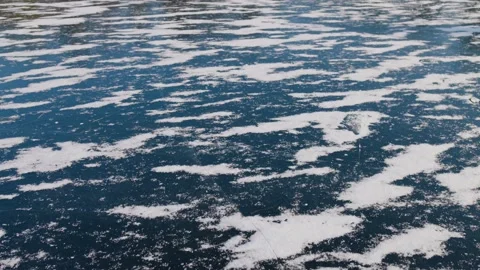 A frozen lake with a layer of ice partially covered by snow. The dark blue Stock-Footage 302982880