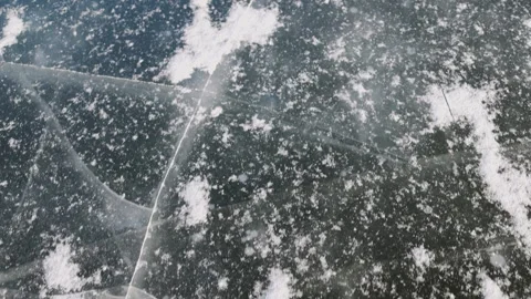 A frozen lake with a layer of ice partially covered by snow. The dark blue Stock Footage 303186620