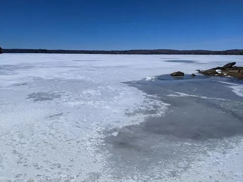 Frozen Lake with Melting Ice Patch Near Rocky Shoreline Fotos Stock
