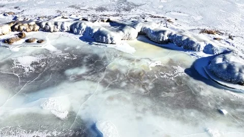 Frozen lake surface with cracked ice and snow-covered rocks on a sunny winter Stock Footage 346305910