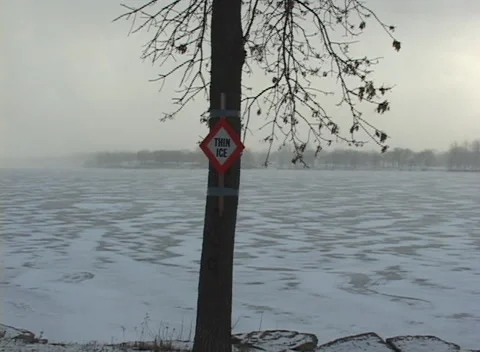 Frozen lake with "thin ice" sign pan L, group of ducks in small open water Video stock 294721789