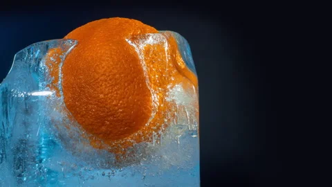 Frozen orange inside a block of ice with blue light melting  Stock Footage 265494898
