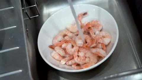 Frozen prawns are thawed under warm tap water in the kitchen Stock Footage 148552974