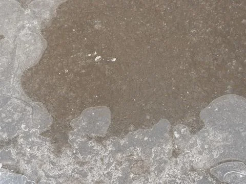 Frozen puddle on the road. close-up. First ice. Slippery Stock Photos