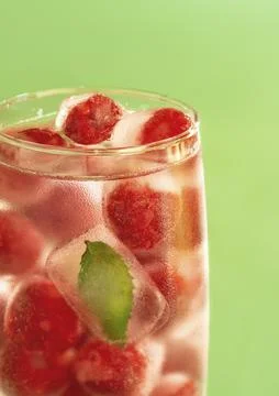 Frozen raspberries and mint leaf in a glass of water on a green background. Stock Photos