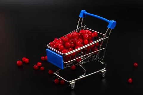 Frozen red currant berries in a small shopping cart on a black background. Stock Photos