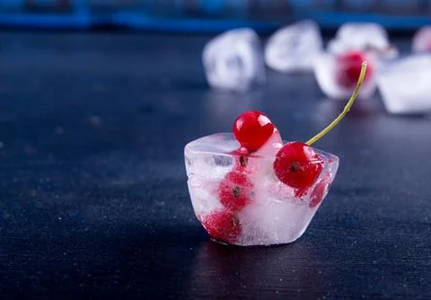 Frozen red currant in ice cube over dark background. Stock Photos