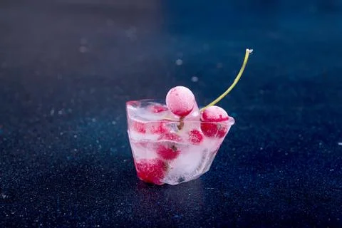 Frozen red currant in ice cube over dark background. Stock Photos