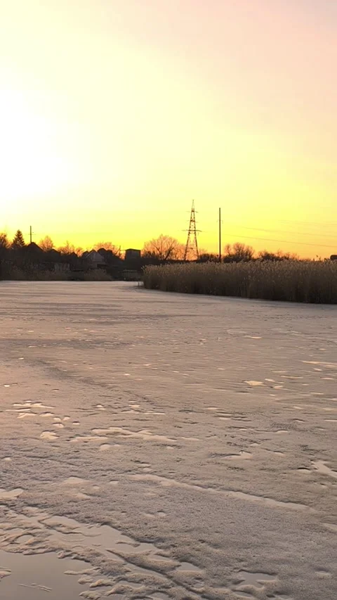 Frozen river covered with textured ice under warm sunset sky near dry reeds and Stock Footage 346041479