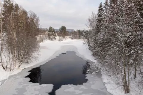 Frozen river with open spot surrounded by trees Stock Photos