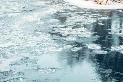 Frozen river surface with thin ice and floating snow patches in winter, cold Stock Photos