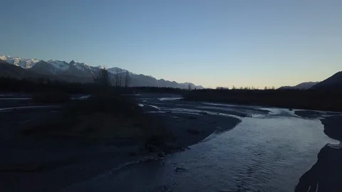 Frozen river surrounded with forest and snow clad mountains at dusk Stock Footage 104532030