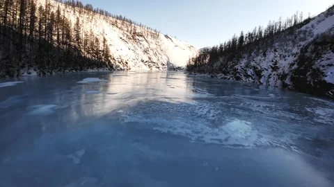Frozen river winding through a snow-covered mountain landscape Vídeos de archivo 334484509