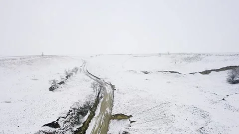 Frozen riverbed surrounded with snow covered hilly land in bright white sky 스톡 동영상 263358343