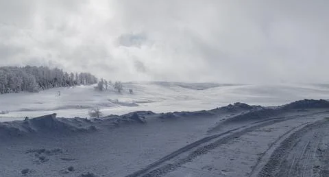 A frozen road with a distant forest in the sunlight, on top of a mountain i.. Foto stock