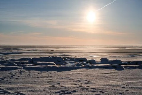 A frozen sea. The sun is setting in the background. The sky is blue and the sun Stock Photos