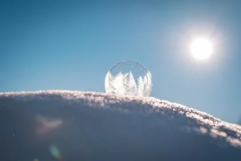 Frozen soap bubble with a beautiful pattern on the snow close up on a blurry Stock Photos