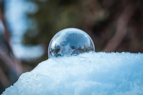 Frozen soap bubble with a beautiful pattern on the snow close up on a blurry Stock Photos