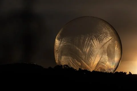 Frozen soap bubble with ice pattern on cold winter day at the sunset. Stock Photos