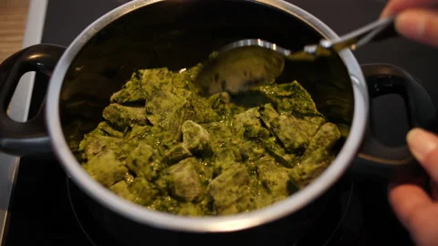 Frozen spinach in small portions is thawed in a black pot on the stove Stock Footage 231933297