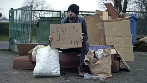 Frozen untidy young man sits by a pile of rubbish and holds a handwritten LOST Stock Footage 249802414